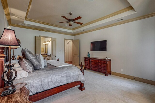 carpeted bedroom featuring crown molding, a tray ceiling, ensuite bath, and ceiling fan