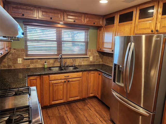 kitchen featuring stainless steel appliances, wood-type flooring, range hood, dark stone counters, and sink