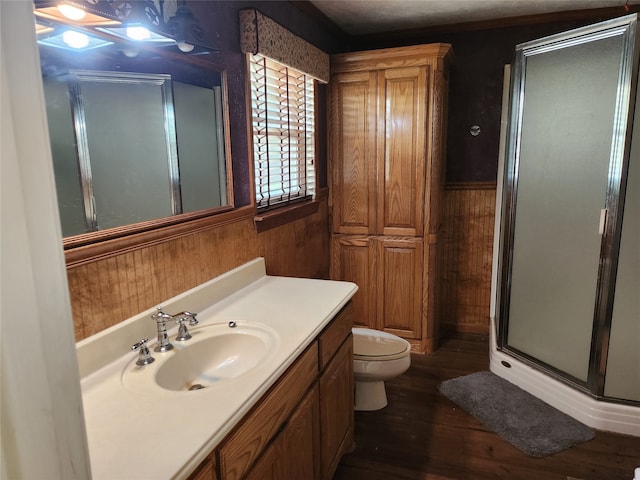 bathroom with vanity, toilet, wooden walls, a shower with shower door, and hardwood / wood-style floors