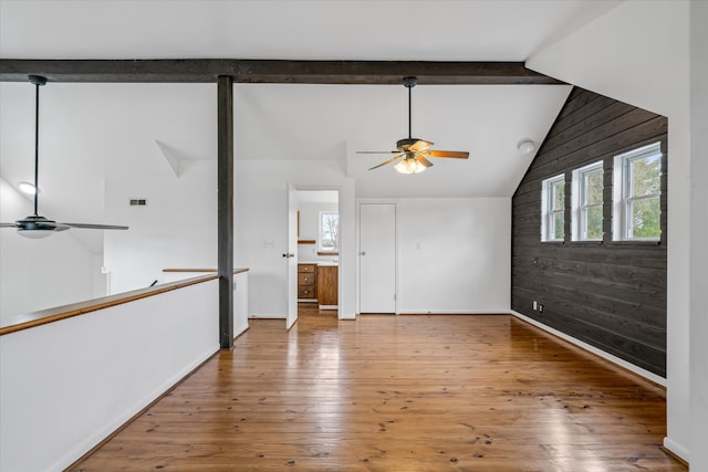 unfurnished living room featuring wood-type flooring, lofted ceiling with beams, wood walls, and ceiling fan