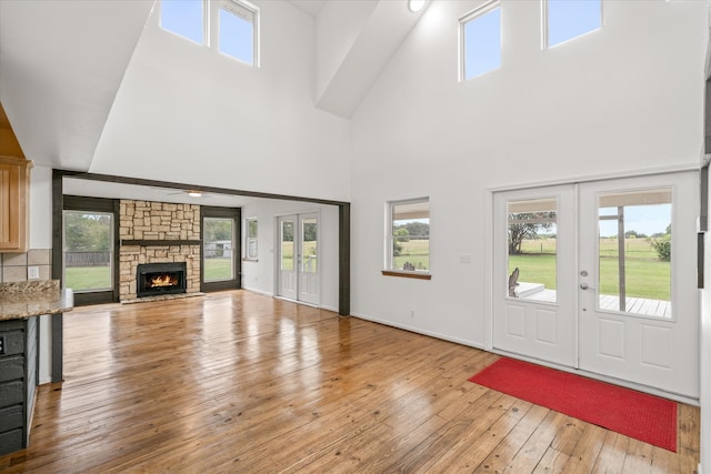 unfurnished living room featuring french doors, a stone fireplace, light hardwood / wood-style flooring, and a towering ceiling