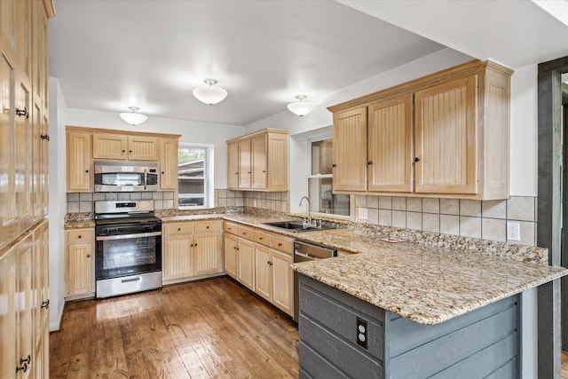 kitchen with appliances with stainless steel finishes, kitchen peninsula, light stone countertops, dark hardwood / wood-style floors, and sink