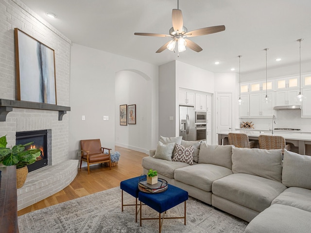 living room featuring ceiling fan, a fireplace, and light wood-type flooring