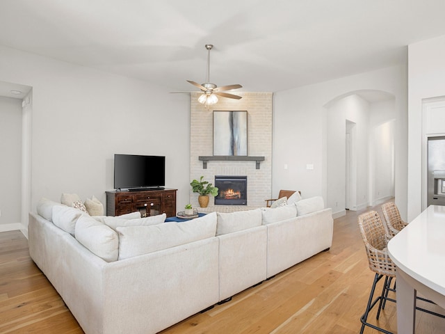 living room with ceiling fan, light hardwood / wood-style flooring, and a brick fireplace