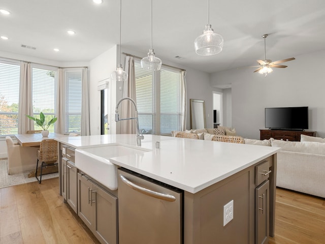 kitchen with sink, hanging light fixtures, stainless steel dishwasher, an island with sink, and light hardwood / wood-style floors