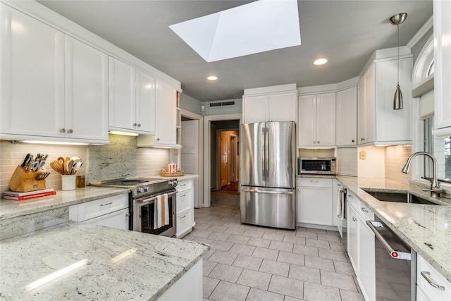 kitchen with white cabinets, light stone countertops, stainless steel appliances, a skylight, and decorative light fixtures