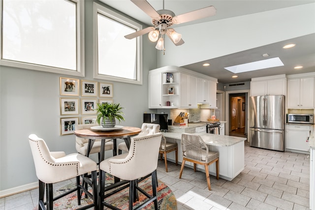 kitchen featuring ceiling fan, white cabinets, a skylight, light stone counters, and stainless steel appliances