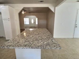 kitchen featuring white cabinets, light stone counters, and ceiling fan