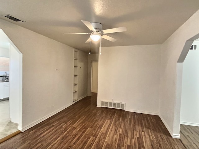 spare room featuring a textured ceiling, ceiling fan, dark wood-type flooring, and built in features