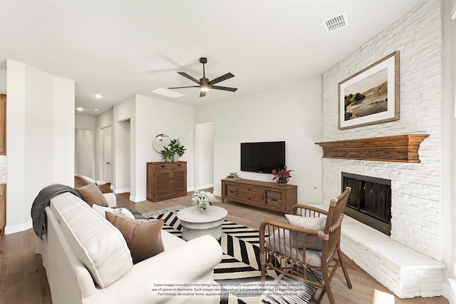 living room with a stone fireplace, ceiling fan, and wood-type flooring