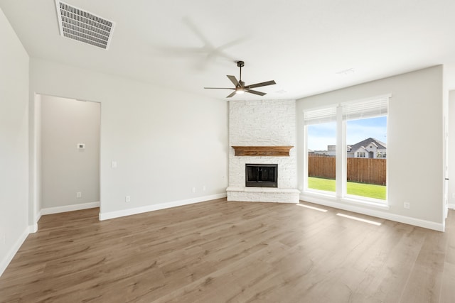 unfurnished living room featuring ceiling fan, a stone fireplace, and wood-type flooring