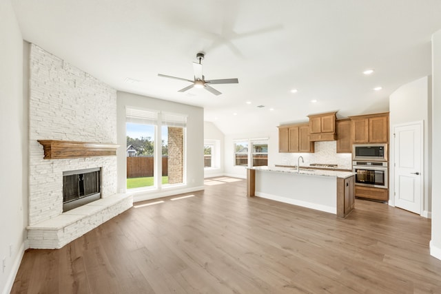 kitchen featuring stainless steel appliances, a stone fireplace, light hardwood / wood-style flooring, an island with sink, and lofted ceiling