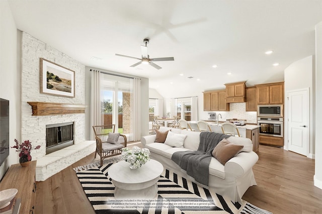 living room with ceiling fan, a fireplace, light hardwood / wood-style floors, and lofted ceiling