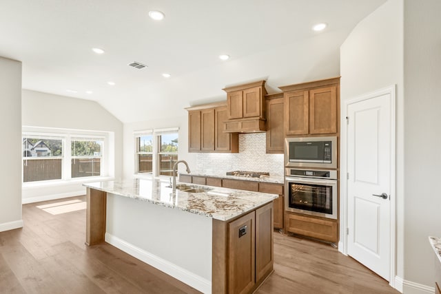 kitchen featuring appliances with stainless steel finishes, vaulted ceiling, sink, light hardwood / wood-style flooring, and an island with sink