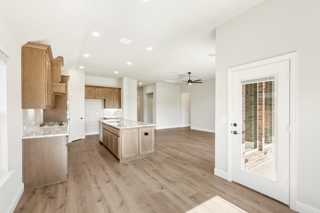 kitchen featuring ceiling fan, sink, light hardwood / wood-style flooring, backsplash, and an island with sink