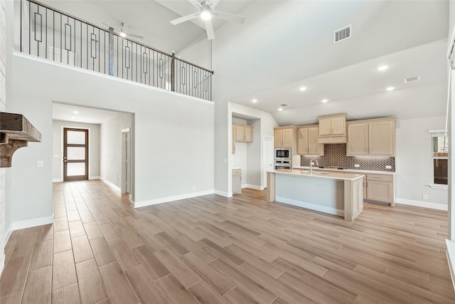 kitchen with an island with sink, high vaulted ceiling, backsplash, appliances with stainless steel finishes, and sink