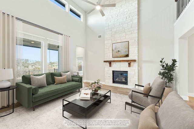 living room with a towering ceiling, ceiling fan, a healthy amount of sunlight, and a stone fireplace