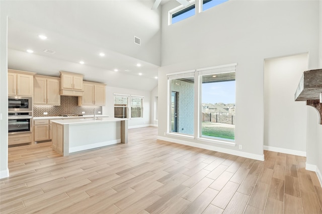 kitchen with appliances with stainless steel finishes, light wood-type flooring, light brown cabinets, a high ceiling, and backsplash