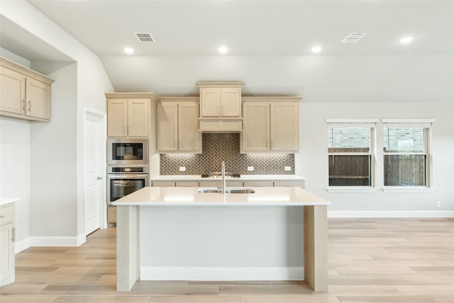 kitchen featuring sink, stainless steel oven, light brown cabinets, a kitchen island with sink, and built in microwave