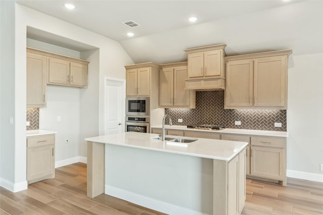 kitchen with light brown cabinetry, a center island with sink, lofted ceiling, appliances with stainless steel finishes, and sink