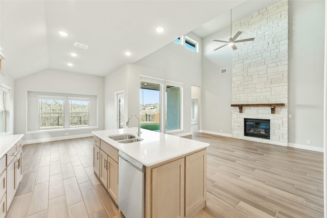 kitchen with stainless steel dishwasher, light brown cabinetry, a kitchen island with sink, a fireplace, and sink