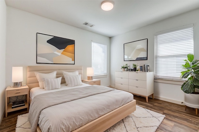 bedroom featuring visible vents, multiple windows, baseboards, and wood finished floors