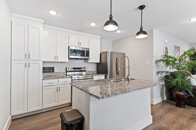 kitchen with appliances with stainless steel finishes, hanging light fixtures, a center island with sink, and white cabinets