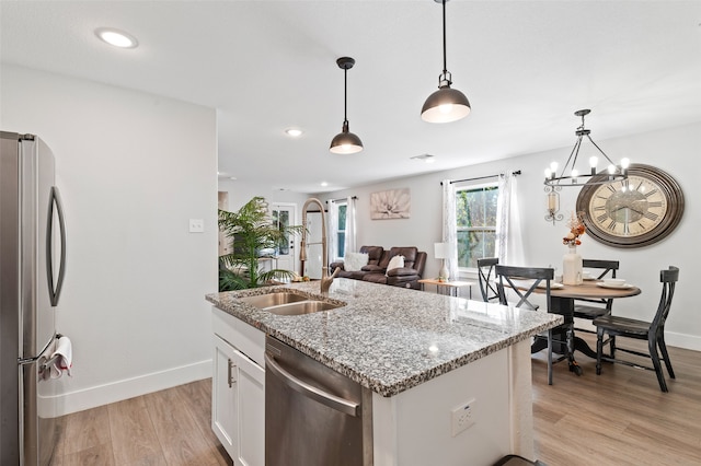 kitchen featuring white cabinets, hanging light fixtures, light hardwood / wood-style flooring, stainless steel appliances, and a center island with sink