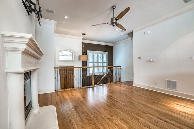 unfurnished living room with ornamental molding, wood finished floors, visible vents, and baseboards