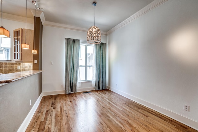 unfurnished dining area featuring baseboards, wood finished floors, visible vents, and crown molding