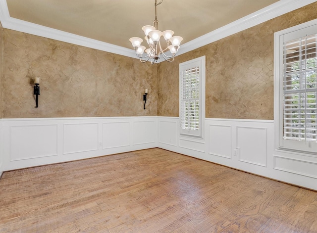 empty room featuring crown molding, wood finished floors, an inviting chandelier, and a wainscoted wall