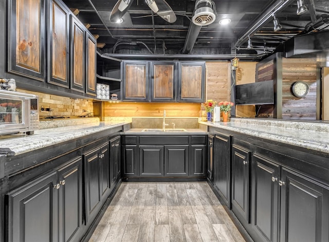 kitchen with light stone countertops, light hardwood / wood-style floors, wooden walls, and sink