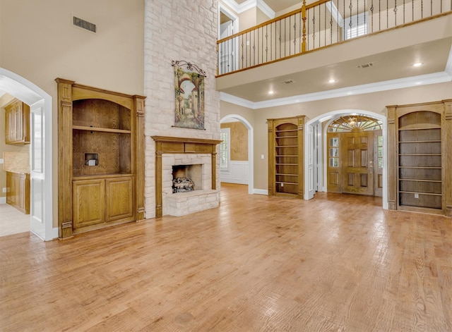 unfurnished living room with a wealth of natural light, a fireplace, a towering ceiling, and light hardwood / wood-style flooring