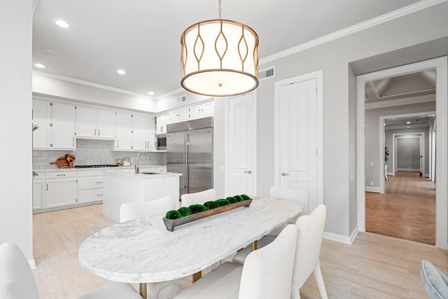 dining room featuring light wood-type flooring, crown molding, and sink