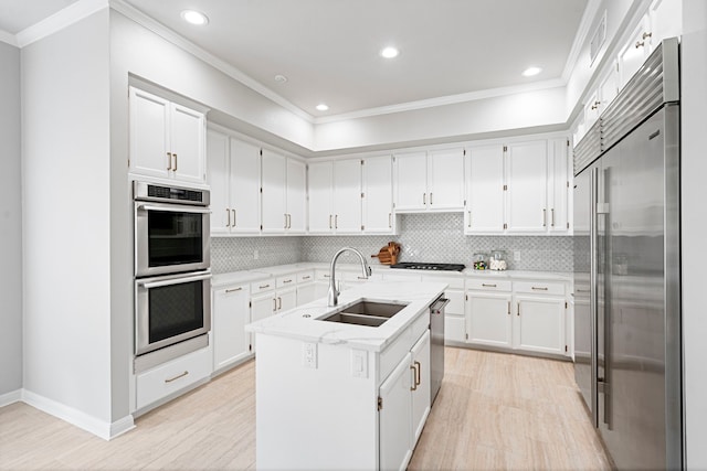 kitchen with white cabinetry, backsplash, stainless steel appliances, a center island with sink, and sink