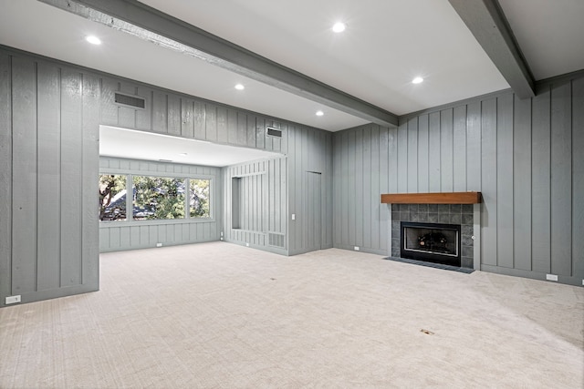 unfurnished living room with wooden walls, beam ceiling, a tiled fireplace, and light colored carpet