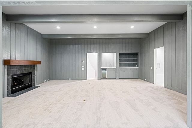 unfurnished living room with beamed ceiling, wooden walls, light wood-type flooring, and a tile fireplace