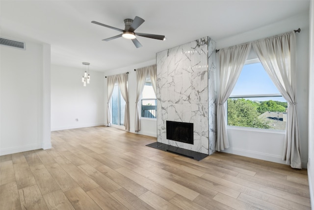 unfurnished living room featuring light wood-type flooring, ceiling fan with notable chandelier, and a high end fireplace