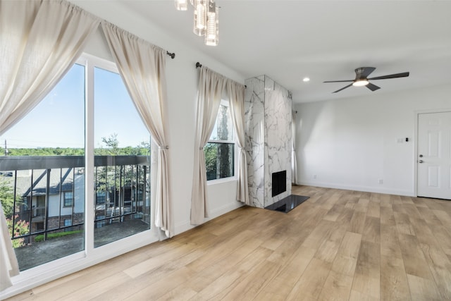 unfurnished living room featuring ceiling fan with notable chandelier, plenty of natural light, a high end fireplace, and light hardwood / wood-style flooring