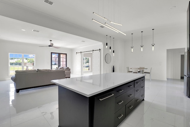 kitchen with hanging light fixtures, a barn door, a kitchen island, light tile patterned floors, and ceiling fan