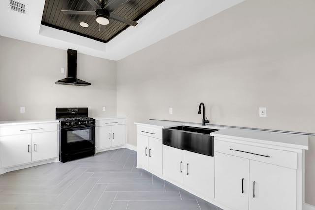 kitchen with white cabinets, wall chimney exhaust hood, ceiling fan, gas stove, and sink