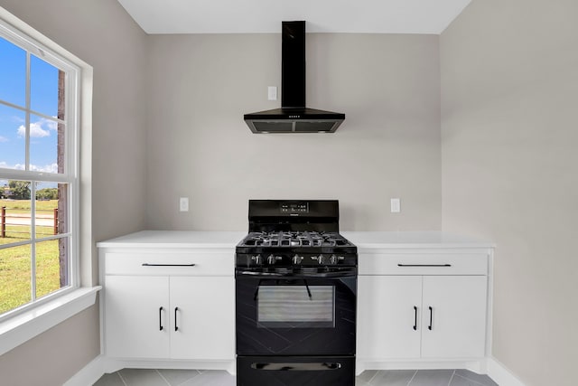 kitchen featuring light tile patterned flooring, black gas stove, wall chimney range hood, and white cabinetry