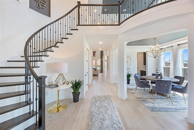 foyer entrance with light wood-type flooring, a towering ceiling, and a chandelier