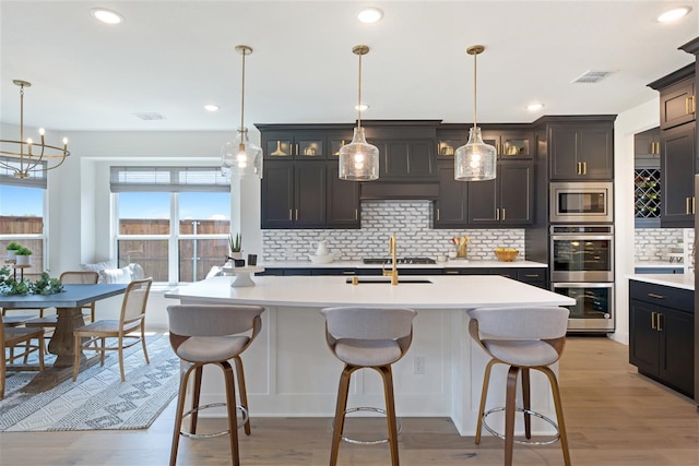 kitchen featuring light hardwood / wood-style floors, a kitchen island with sink, pendant lighting, and tasteful backsplash