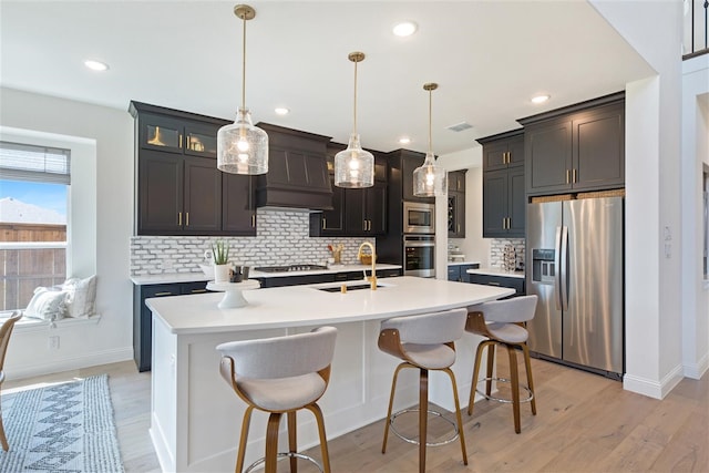 kitchen with custom exhaust hood, an island with sink, sink, decorative light fixtures, and appliances with stainless steel finishes