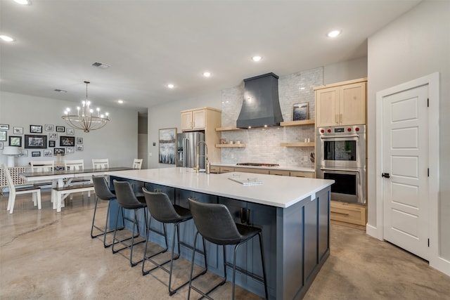 kitchen with premium range hood, a large island with sink, decorative light fixtures, appliances with stainless steel finishes, and a notable chandelier