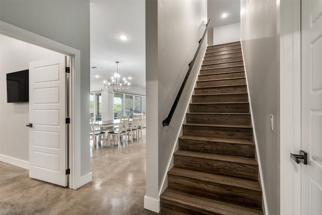 stairway with concrete flooring and an inviting chandelier