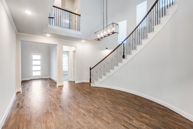 entryway featuring wood-type flooring, a towering ceiling, ornamental molding, and a chandelier