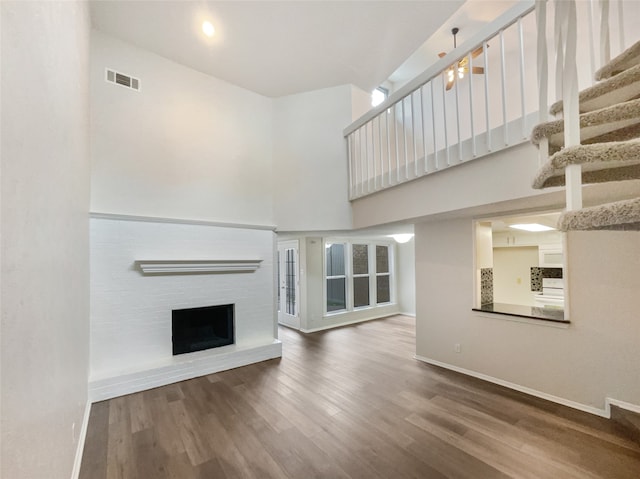 unfurnished living room with a fireplace, a towering ceiling, and hardwood / wood-style floors