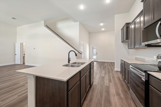 kitchen with a kitchen island with sink, sink, hardwood / wood-style flooring, appliances with stainless steel finishes, and dark brown cabinets